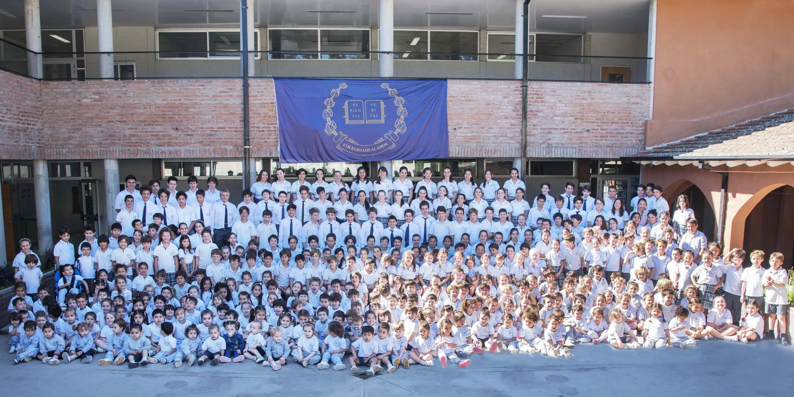 Todos los alumnos del colegio, de maternal a secundario, reunidos en el patio central bajo la bandera con el escudo institucional