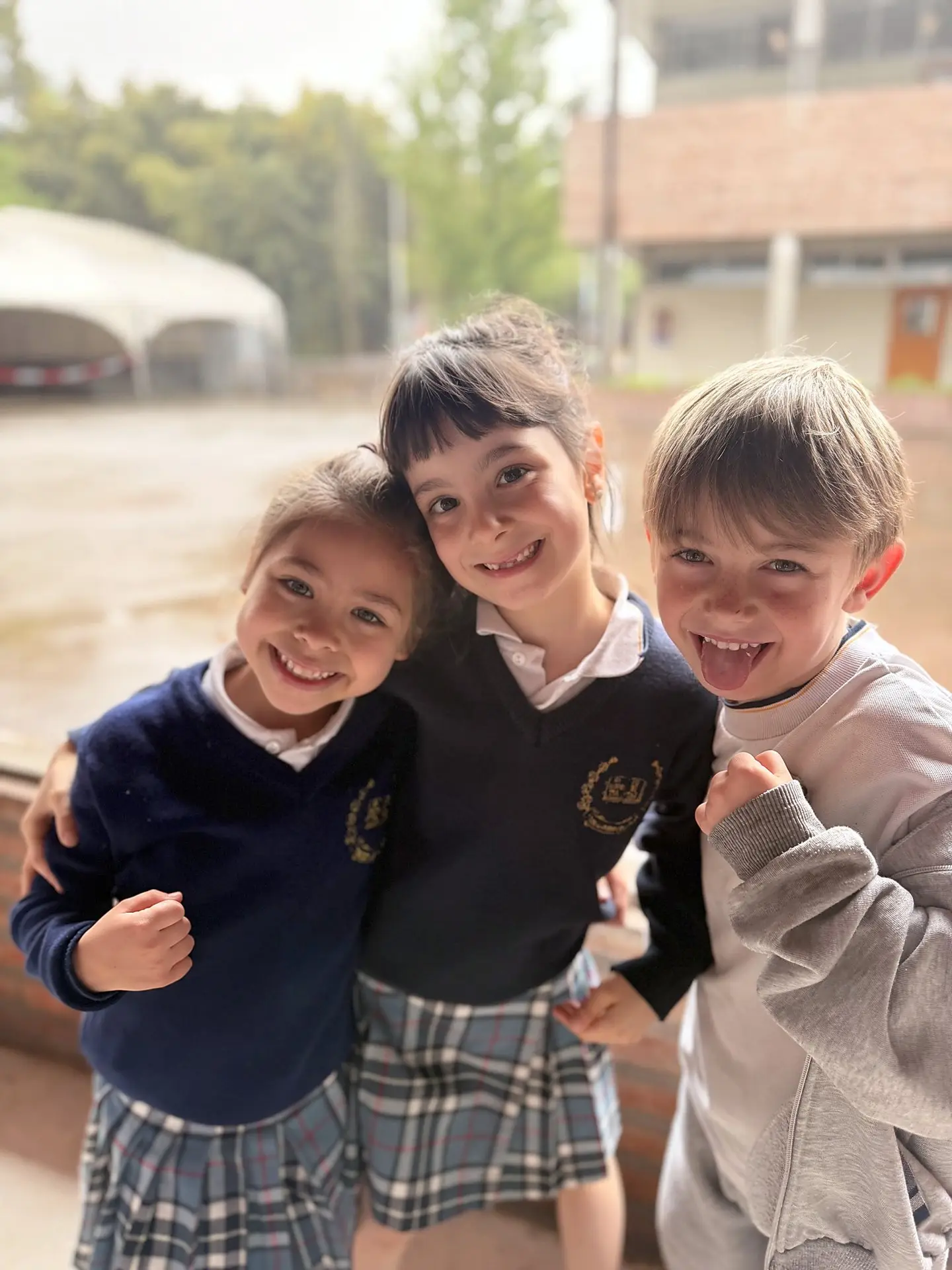 Tres alumnos sonrientes con el uniforme del colegio y el escudo bordado en el buzo