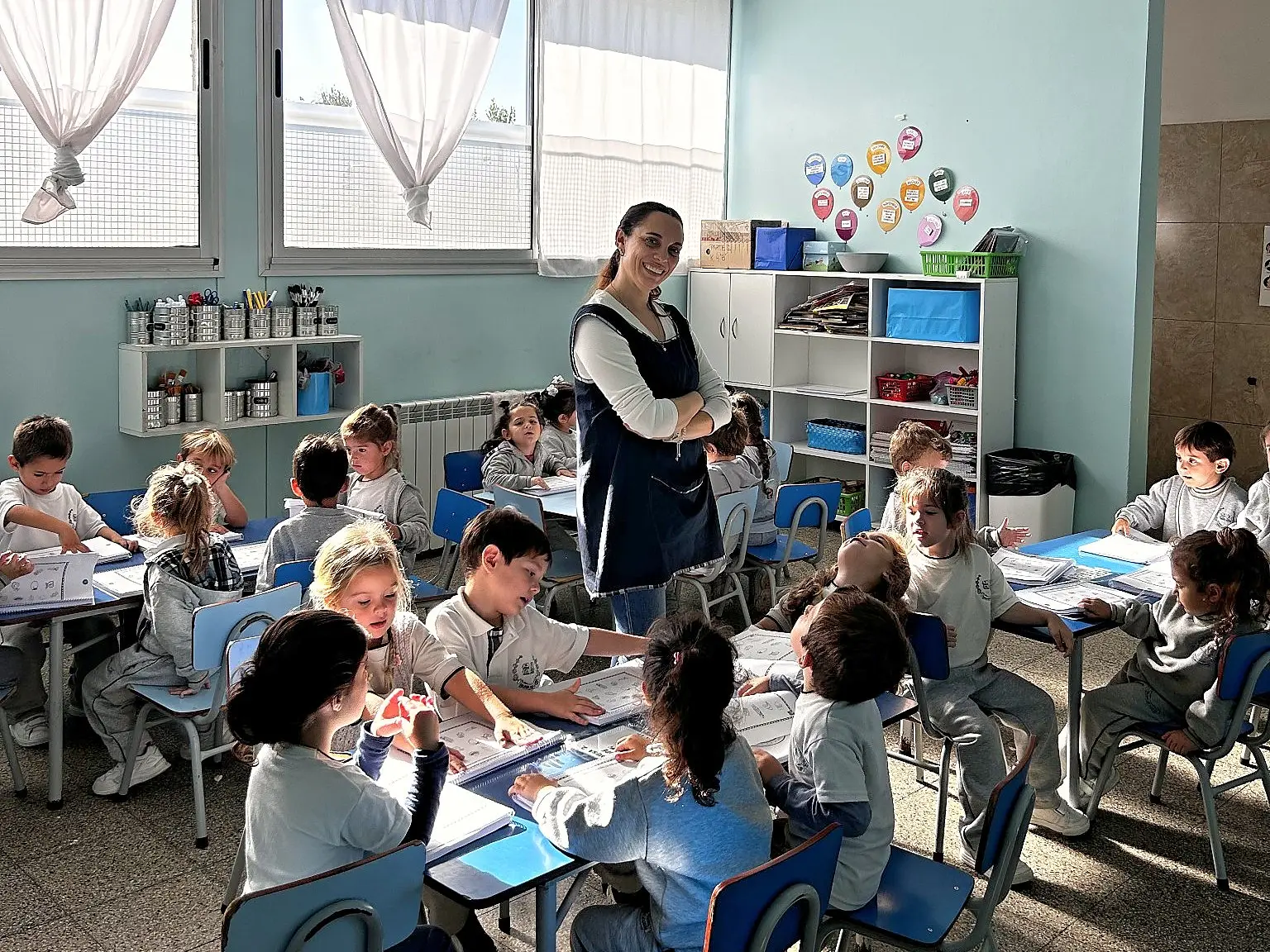 Docente acompañando a alumnos de nivel inicial que trabajan en sus mesas del aula