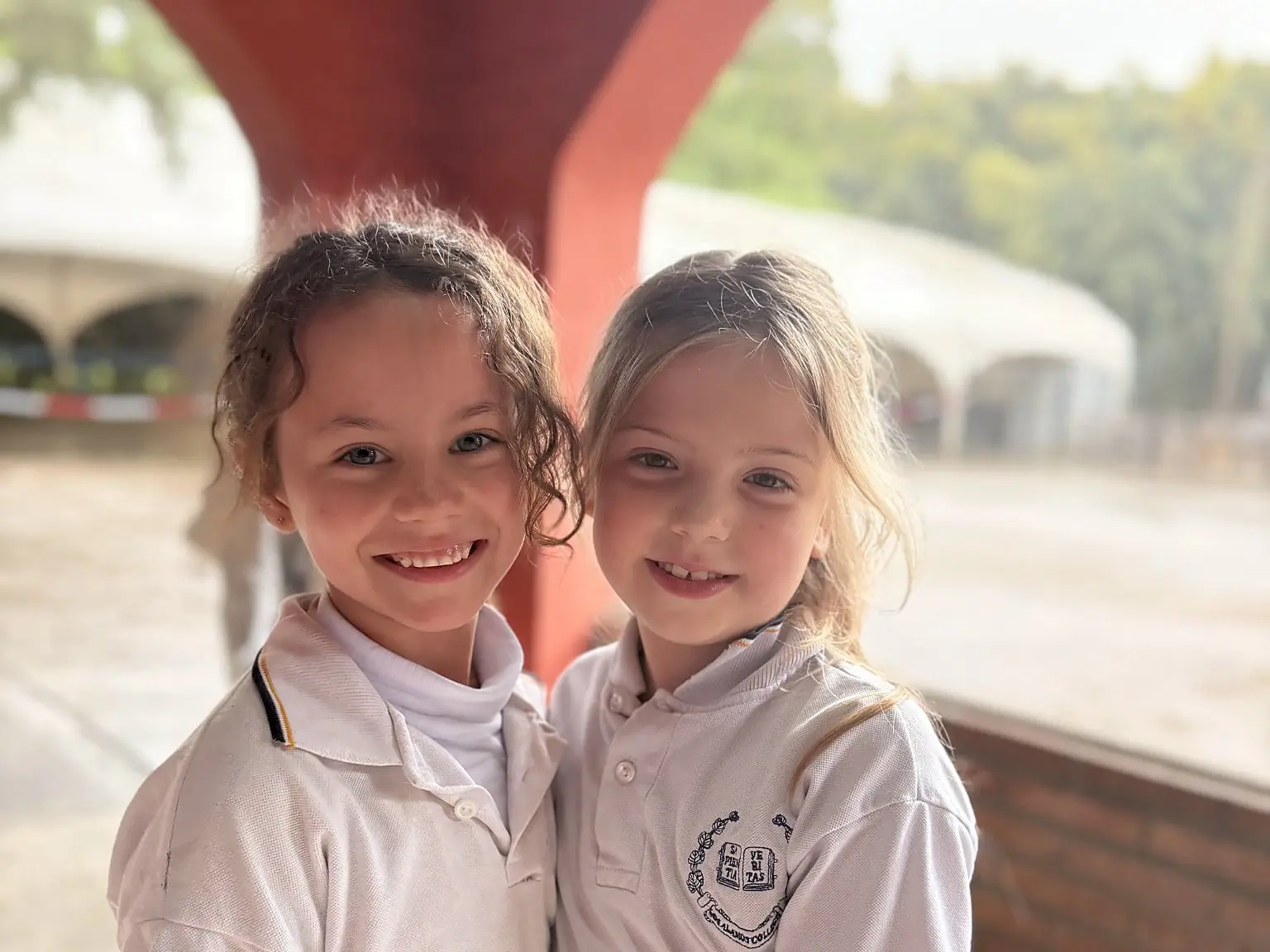 Dos alumnas de primaria abrazadas y sonriendo bajo los arcos del colegio